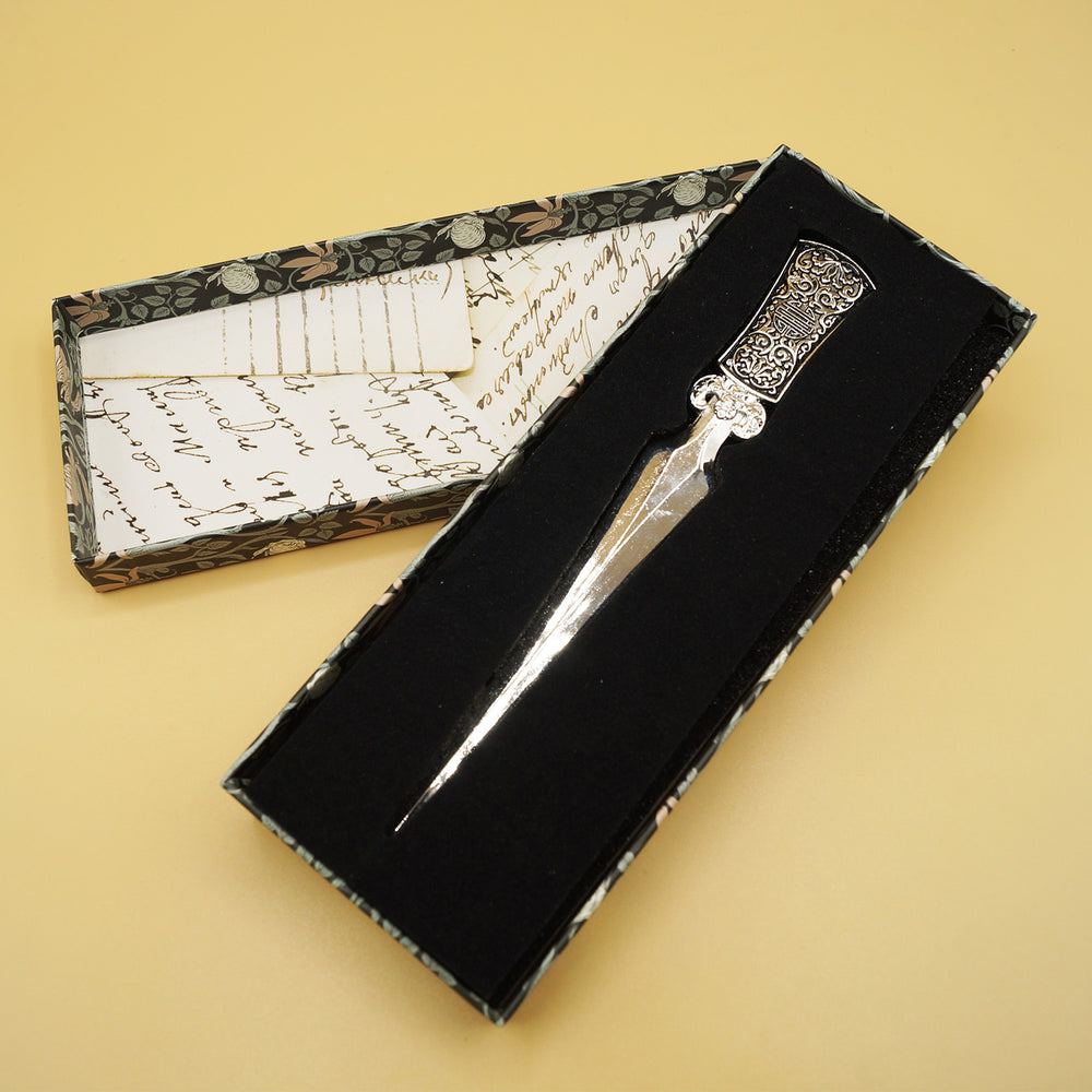 a silver letter opener with intricate design on the handle lays in a box