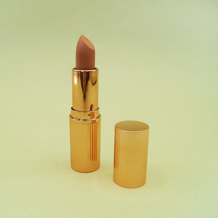 a lipstick tube is open and shows a nude color lipstick, the gold cap is next to it