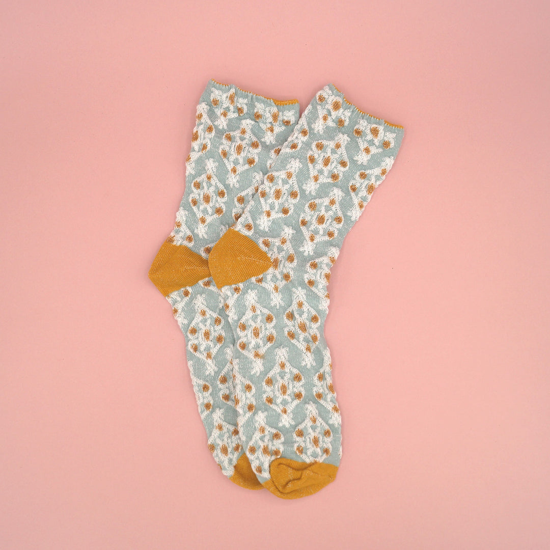 A pair of light blue socks with a gold and white pattern on them.