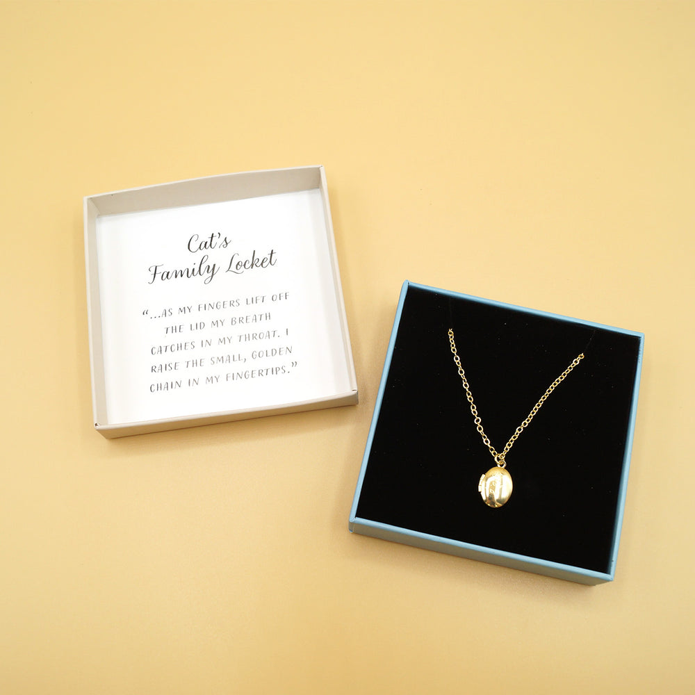 a gold miniature locket necklace in a box against a yellow background