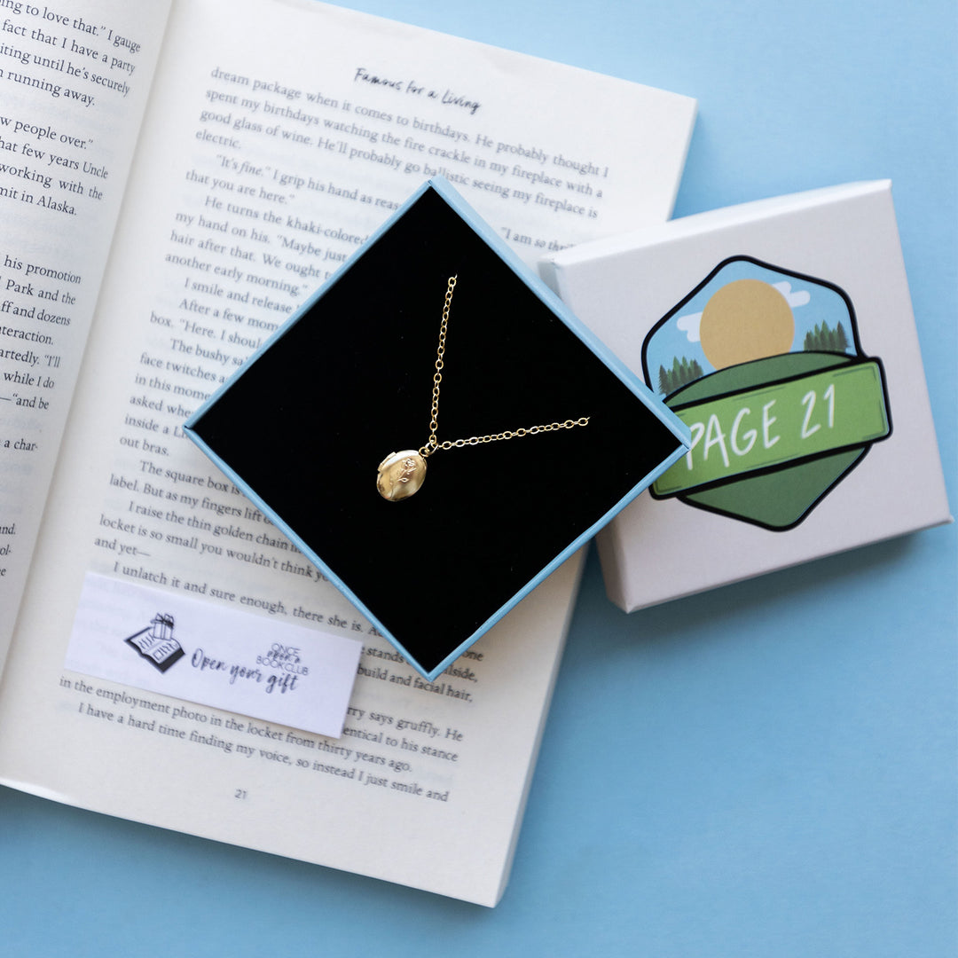a gold miniature locket necklace in a box on top of an open book