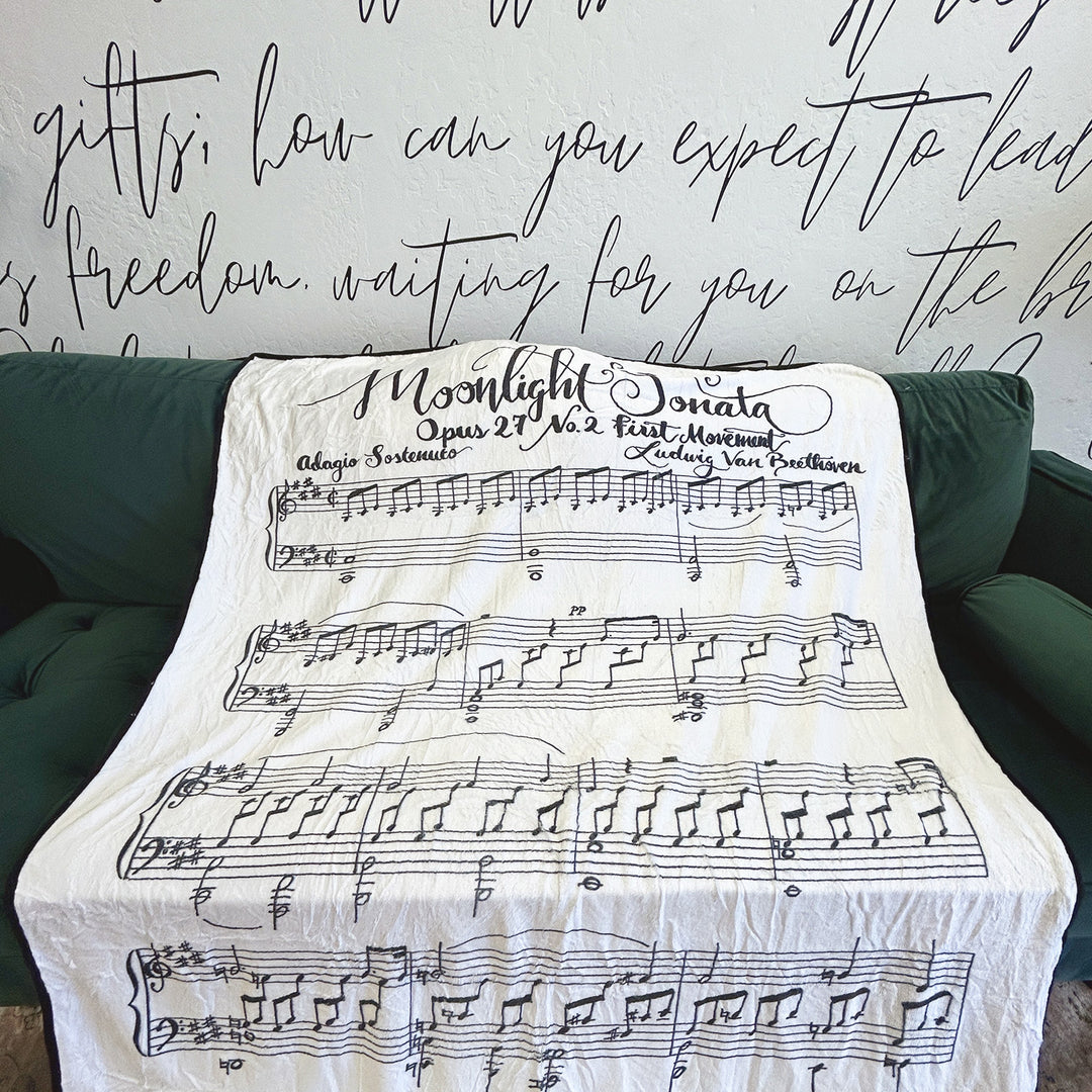 A white fleece blanket featuring Beethoven's Moonlight Sonata lays across a green couch