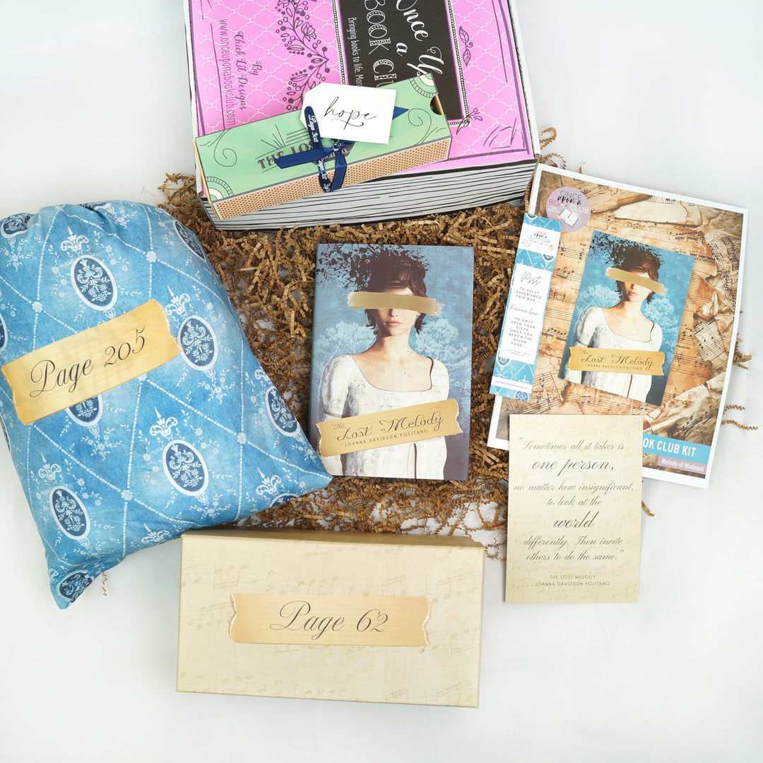 A hardcover special edition of The Lost Melody is centered in the photo, surrounded by a pink box with a rectangular box on top, a blue drawstring bag, a rectangular box, quote card, bookclub kit, and bookmark. The boxes and bags all have page numbers.