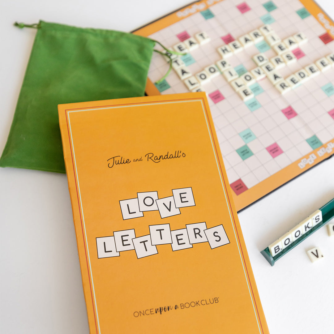 A box in the foreground is labeled Julie and Randall's Love Letters - Once Upon a Book Club. In the background is an open game board with letter tiles spelling out words.