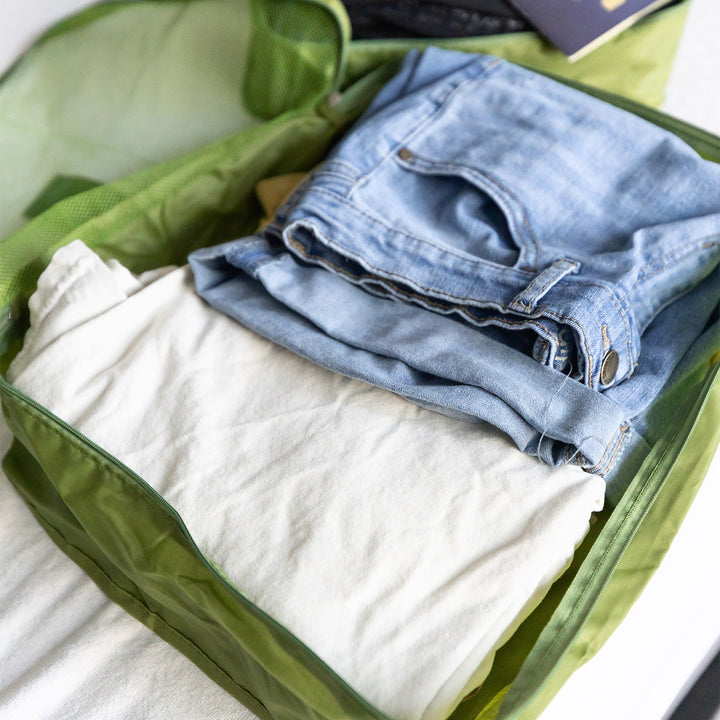 An open, green luggage organizer containing a shirt and pair of jeans.