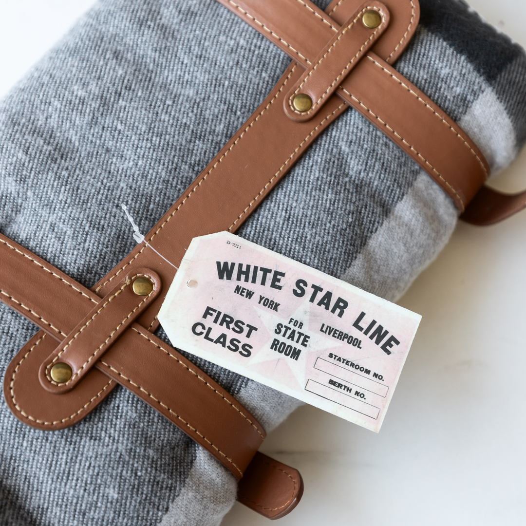 A secured blanket wrapped with faux leather straps. The tag inspired by the White Star Line luggage tags from the Titanic is visible in the image.