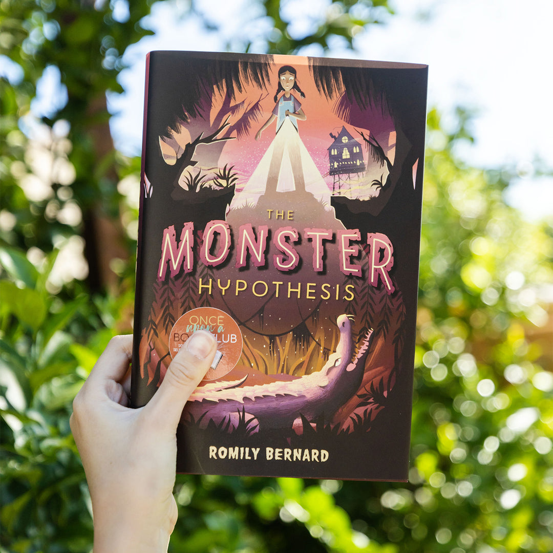 a white hand holding a hardcover edition of The Monster Hypothesis by Romily Bernard against a blurry background
