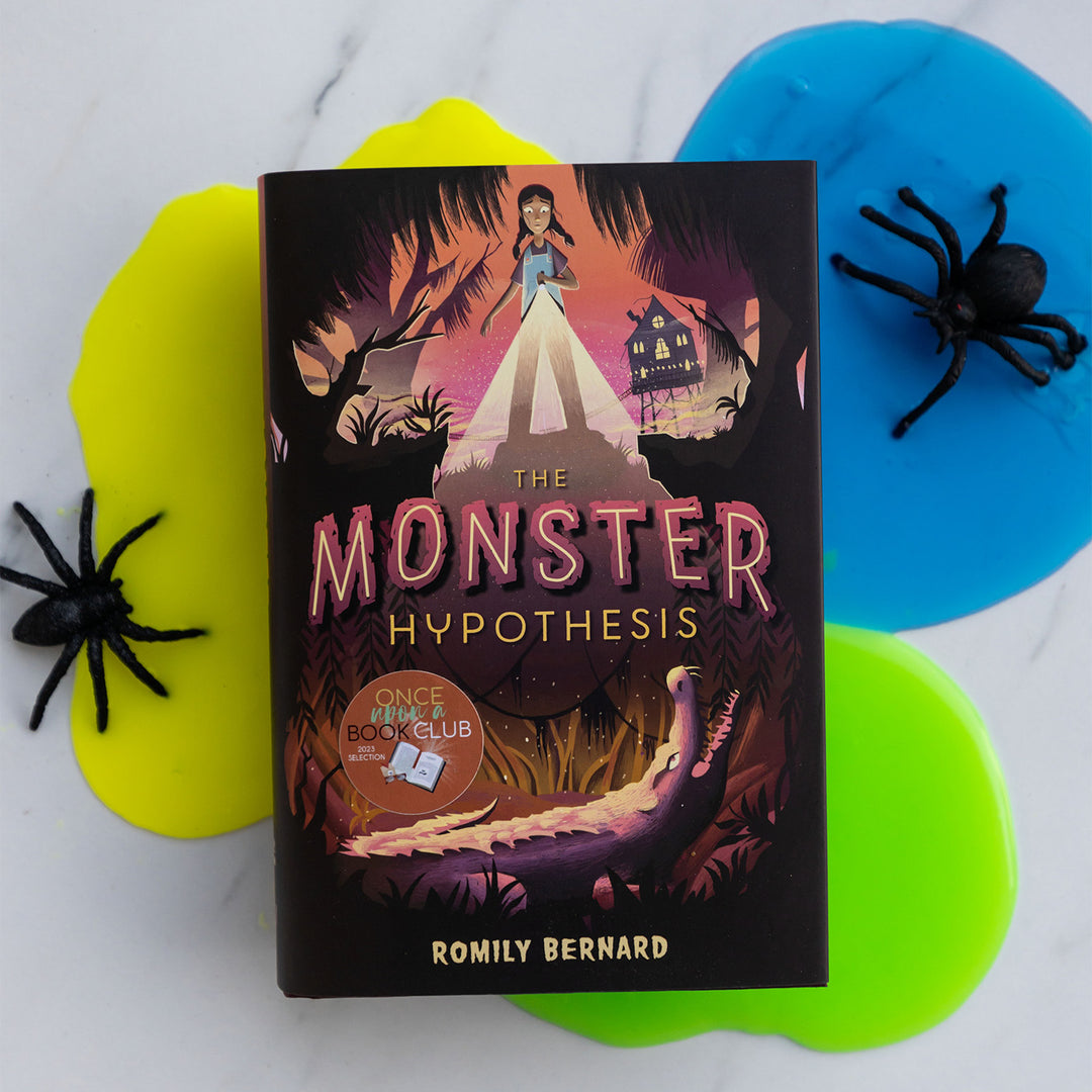 hardcover edition of The Monster Hypothesis by Romily Bernard on top of yellow, blue, and green slime and black fake spiders