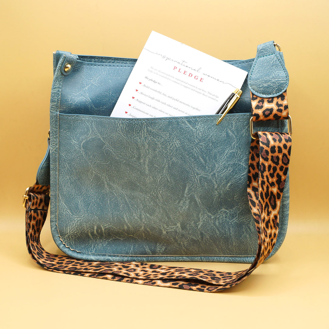 a blue faux leather bag with leopard print strap. a notepad and pen are sticking out of the back pocket
