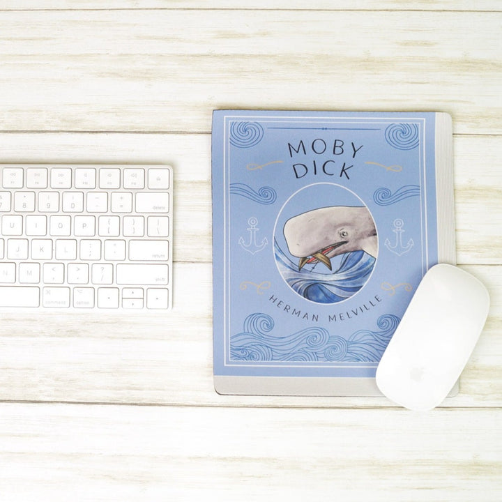 Moby Dick-themed mousepad with a whale illustration, placed on a desk with a keyboard and mouse.