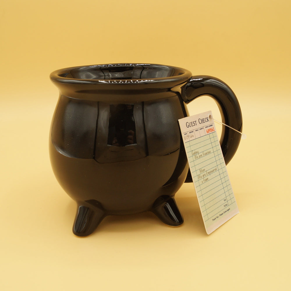 a small piece of paper labeled Guest Check with check-in information on it sits against a black cauldron-shaped mug