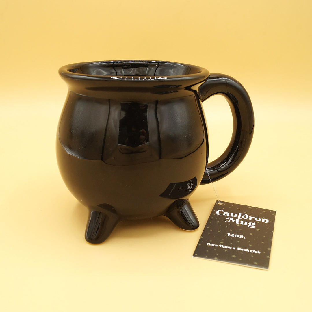 A black cauldron-shaped mug sits against a yellow background