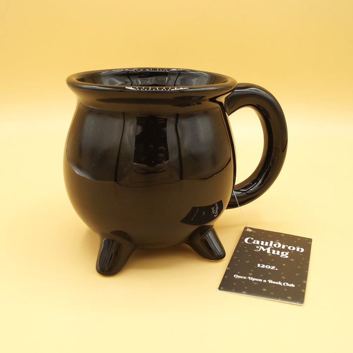 A black cauldron-shaped mug sits against a yellow background