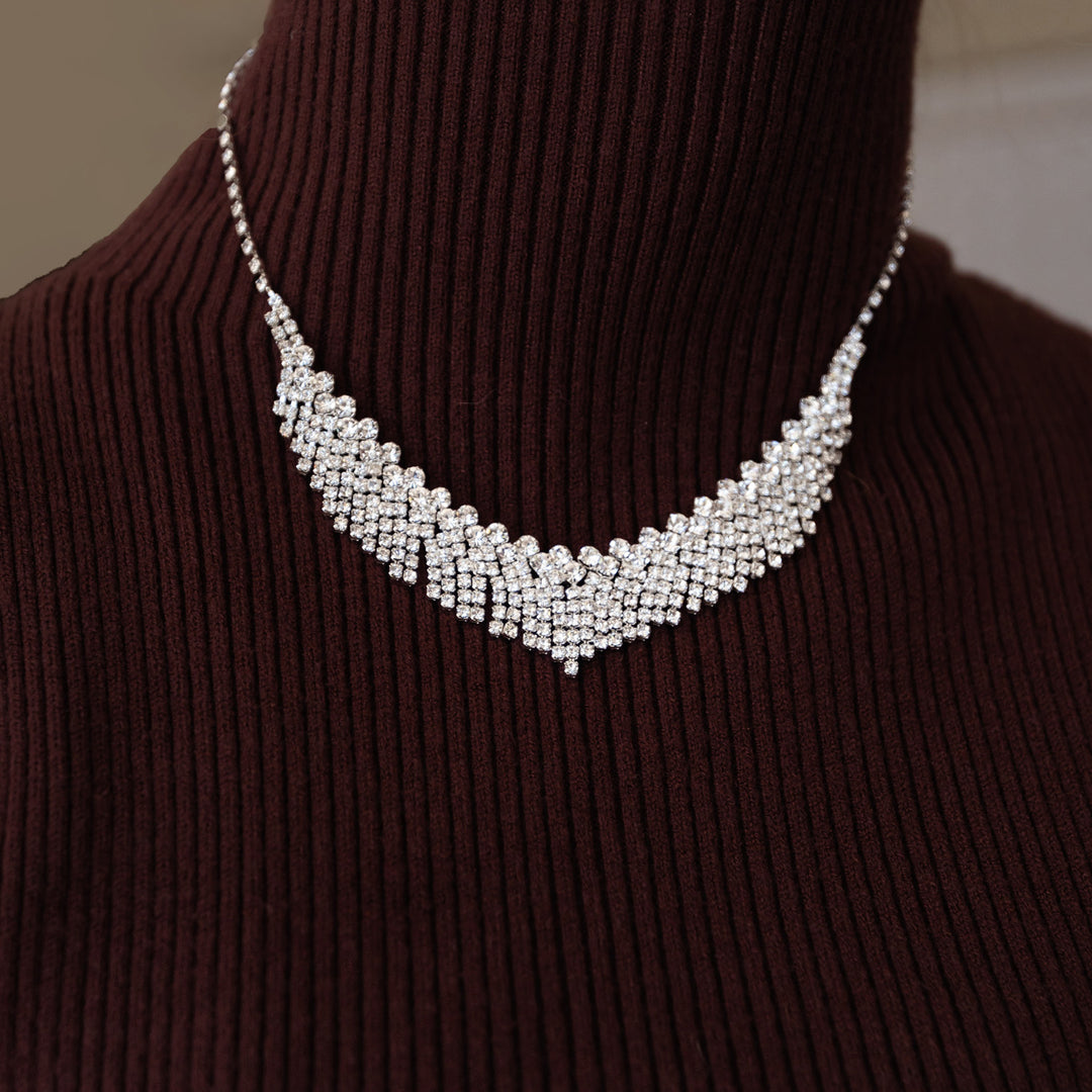 A silver plated necklace clasped around a neck wearing a sweater.