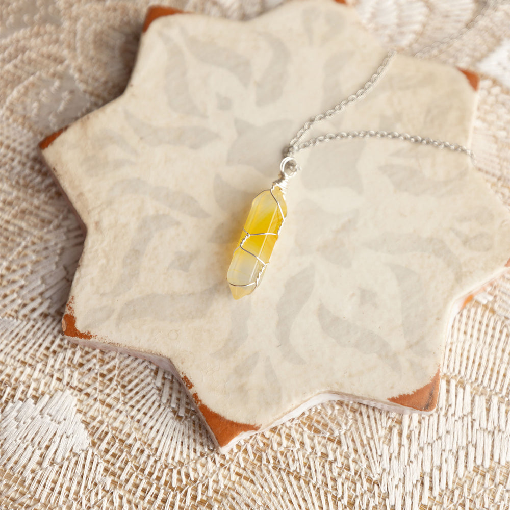 A yellow and clear crystal wrapped in silver wire on a silver chain sits on a star shaped surface.