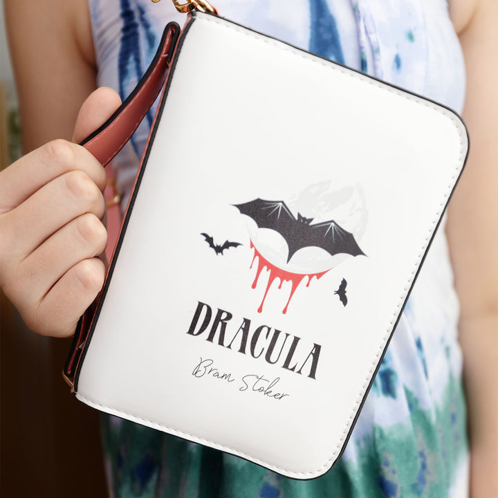 a white hand holds a white purse with images of bats and blood on it and the words Dracula - Bram Stoker