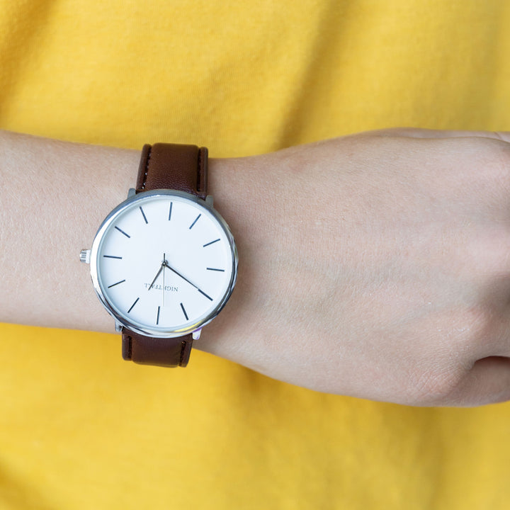 a white arm wearing a brown wristwatch with a white clockface