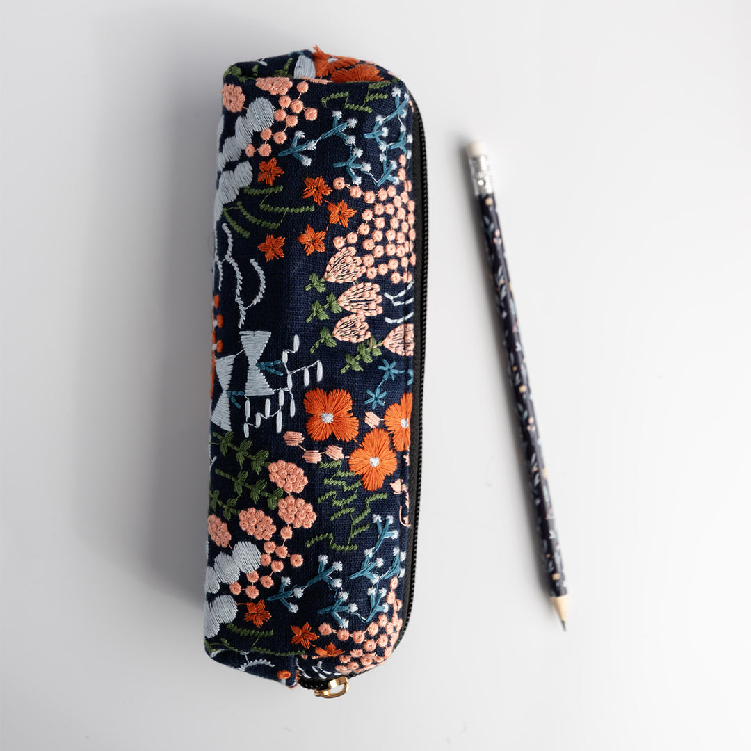 A navy blue pencil pouch with an embroidered floral pattern next to a matching pencil.