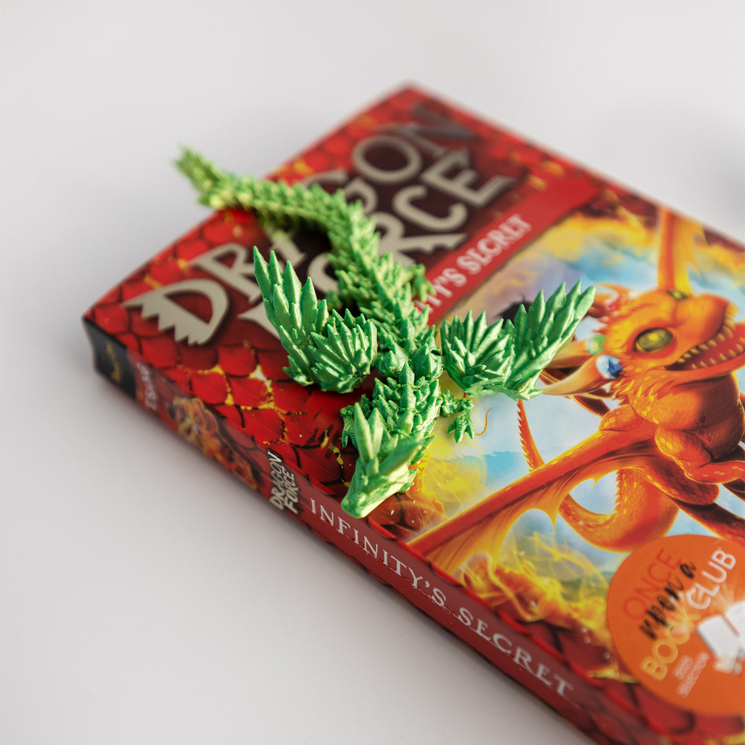 A neon green 3D-printed dragon lays on a paperback edition of Dragon Force: Infinity's Secret.