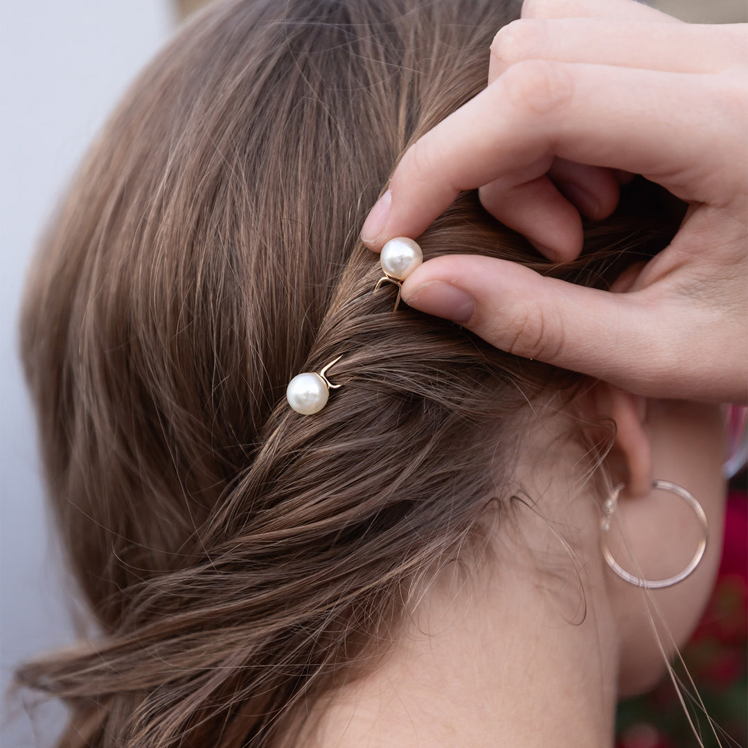 A hand puts two pearl hair pins in a girl's brunette hair.