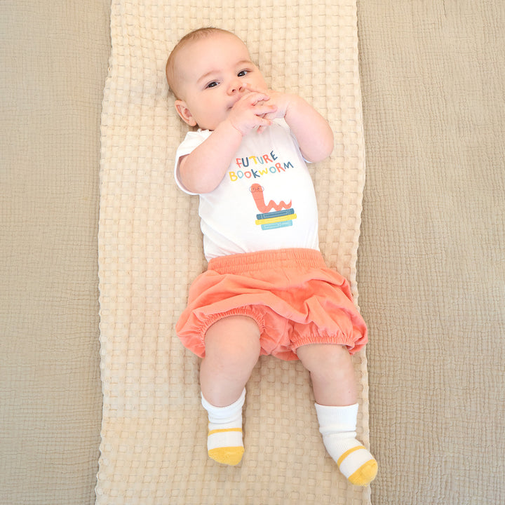 Baby lying on a textured blanket wearing a 'Future Bookworm' shirt and orange shorts.