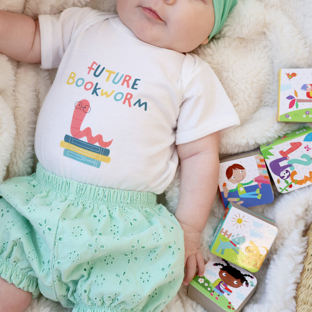 Baby wearing a 'Future Bookworm' shirt surrounded by children's books on a soft surface