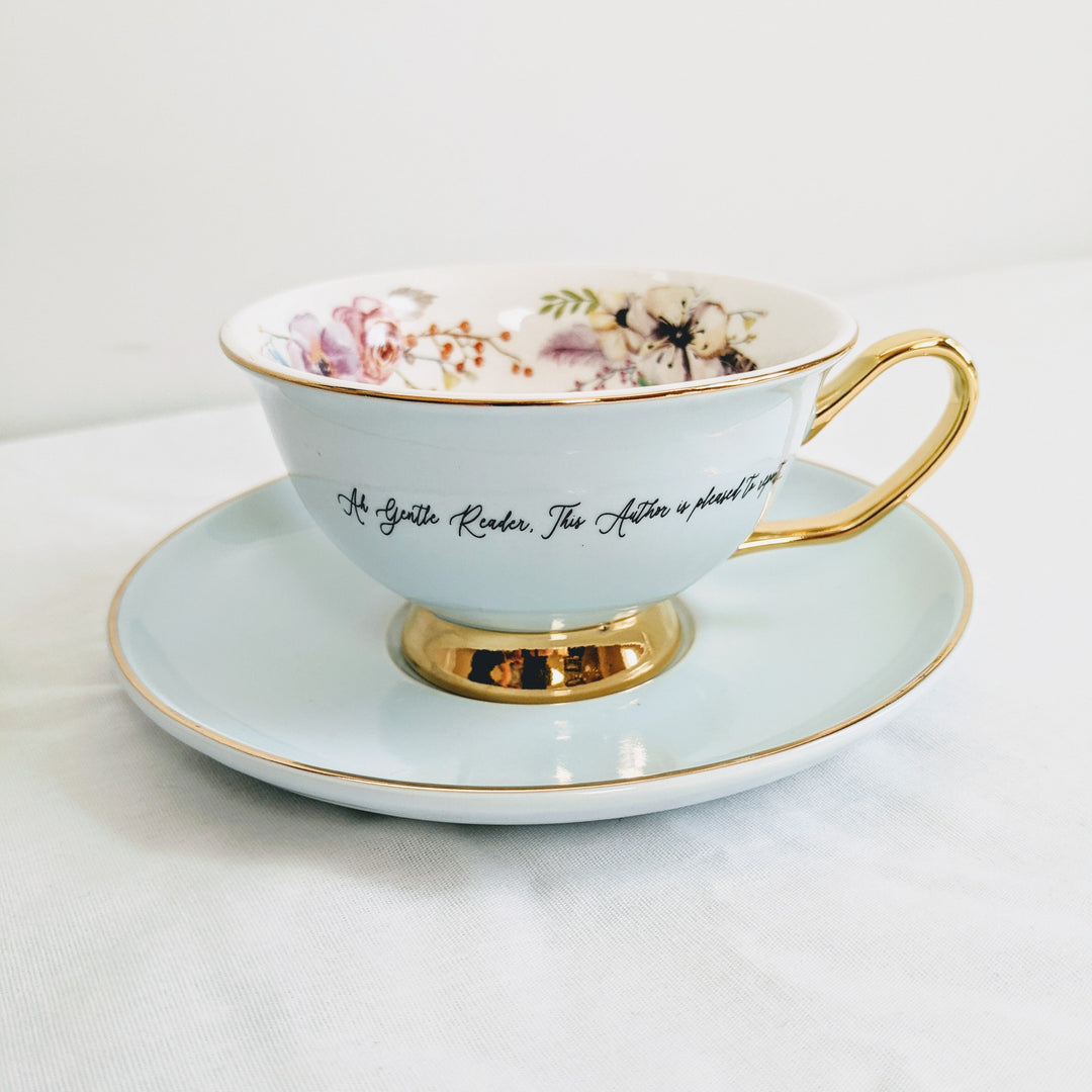 a light blue teacup with gold detail and a quote printed on the outside of it with floral details printed on the inside.