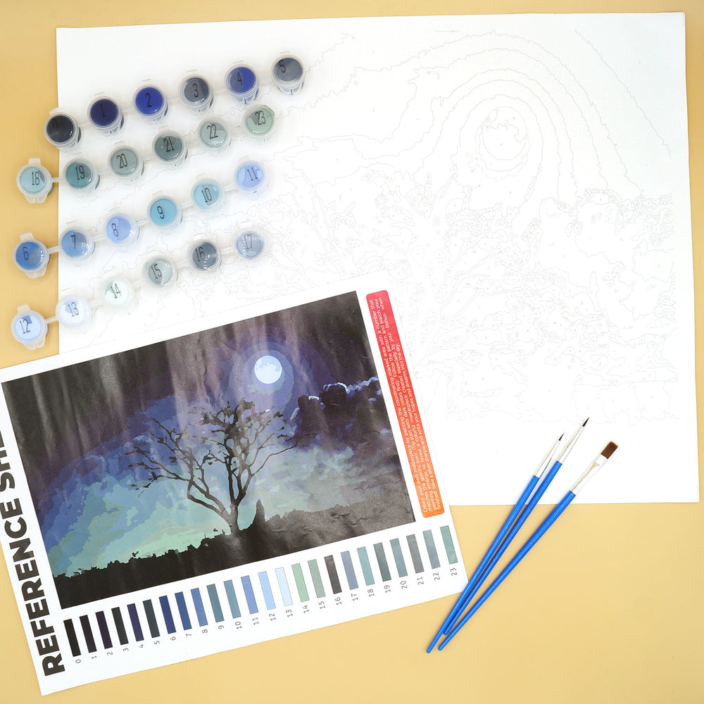 a paint by number kit with a large white paper, multiple sets of paints, reference image of a moonlit tree, and 3 paintbrushes