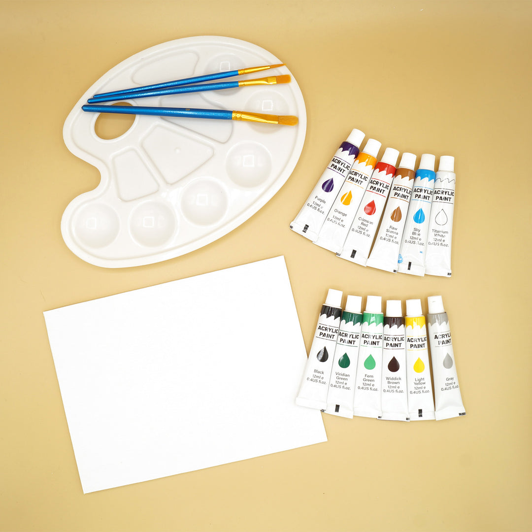 a white canvas and white painter's palette with 3 paint brushes on it are next to 12 paint tubes