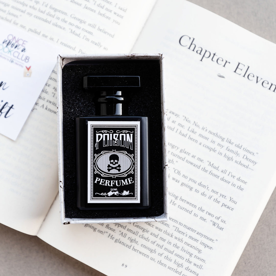 a black perfume bottle labeled Poison Perfume with an image of a skull in the middle is in a box on an open book