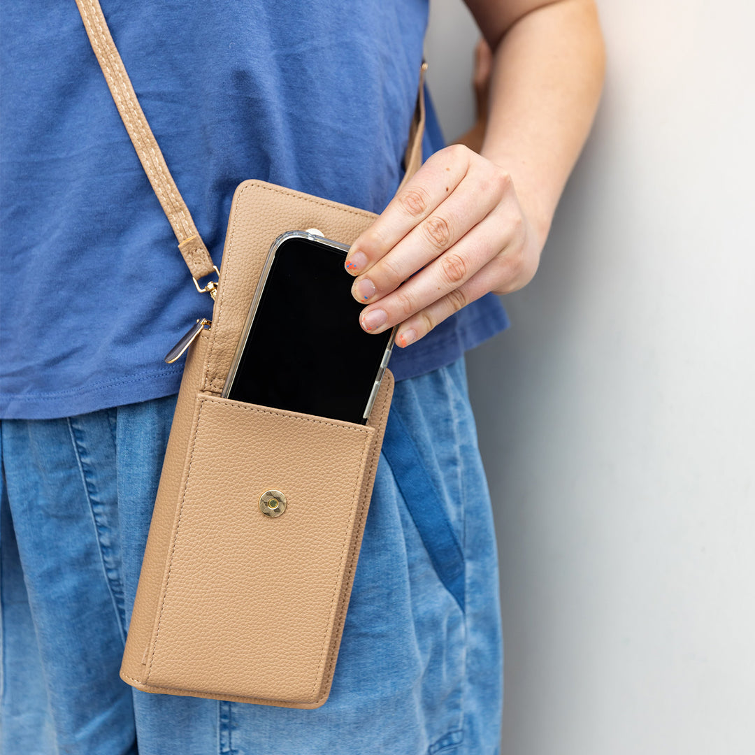 A light brown faux leather crossbody phone wallet with an iPhone half pulled out of it.