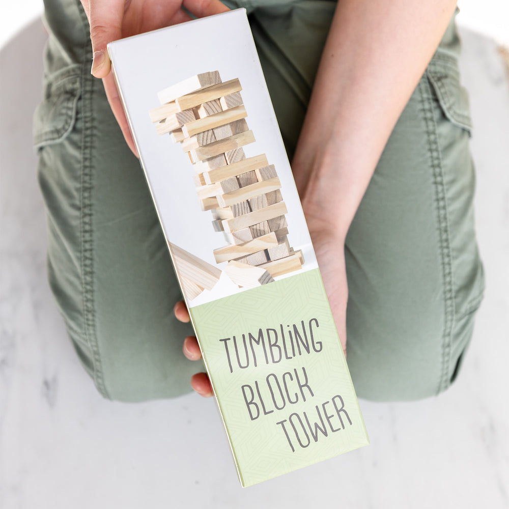 A pair of white hands holds the Tumbling Block Tower game box.