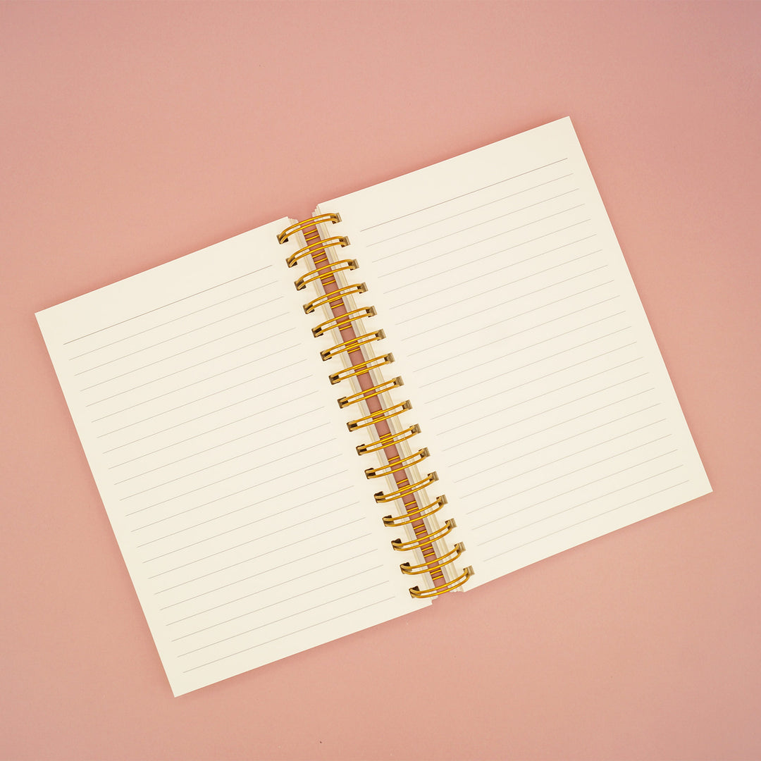 A lined notebook sits open on a pink background to show the interior pages.
