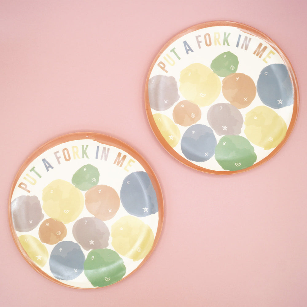 The set of two multi-colored plates sits on a pink background.
