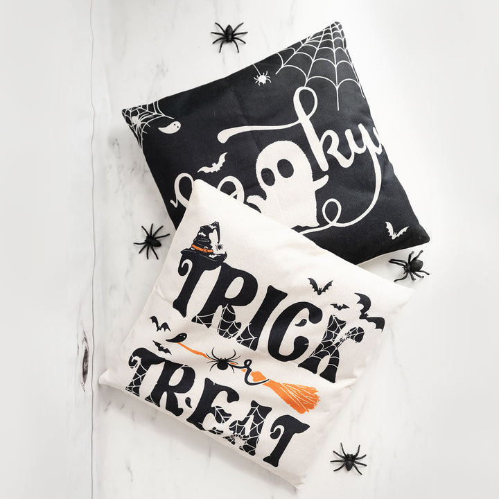 A black pillowcase with the word spooky on it is under a white pillow case with the phrase trick or treat on it. The pillowcases are on a white background with four black fake spiders around them
