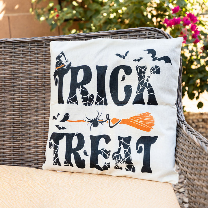 A white pillow sits on a couch outside with the phrase Trick or Treat in black letters with white cobwebs around the words. An orange broomstick is in the middle of the pillow with the word "or" over it