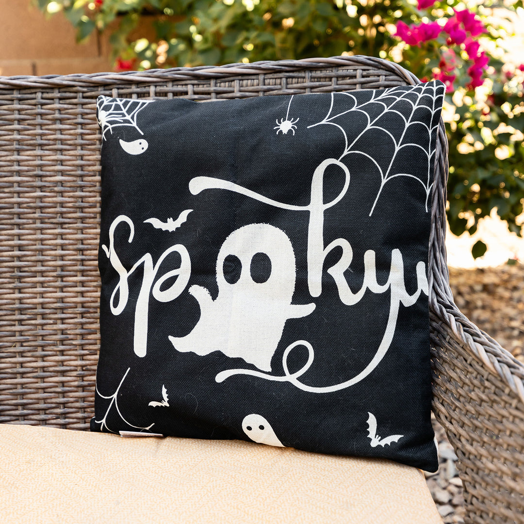 a black pillow sits on a couch outside with a white ghost in the middle of the word Spooky. White cobwebs are on the top corners of the pillow and the bottom left
