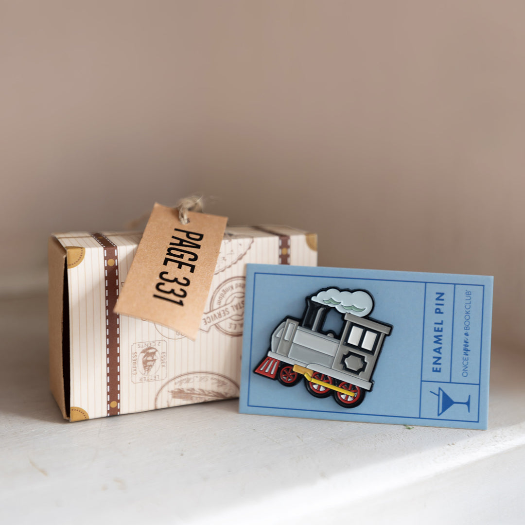 A train-shaped enamel pin next to a box shaped like a suitcase with a tag that says Page 331.