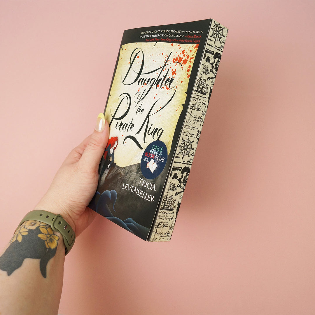 Book titled 'Daughter of the Pirate King' held by a hand on a pink background