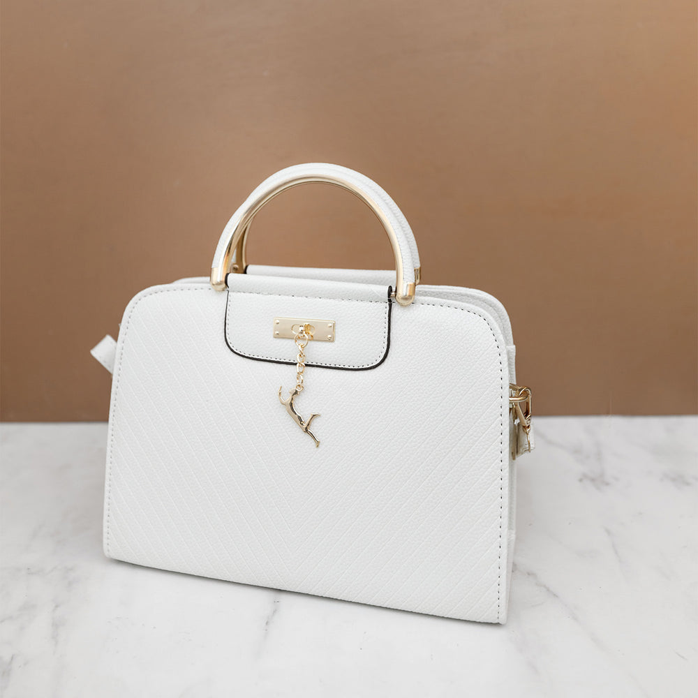 A white marble floor. A brown background. A white rectangular satchel purse sits on the marble flooring. A gold charm hangs from the front.