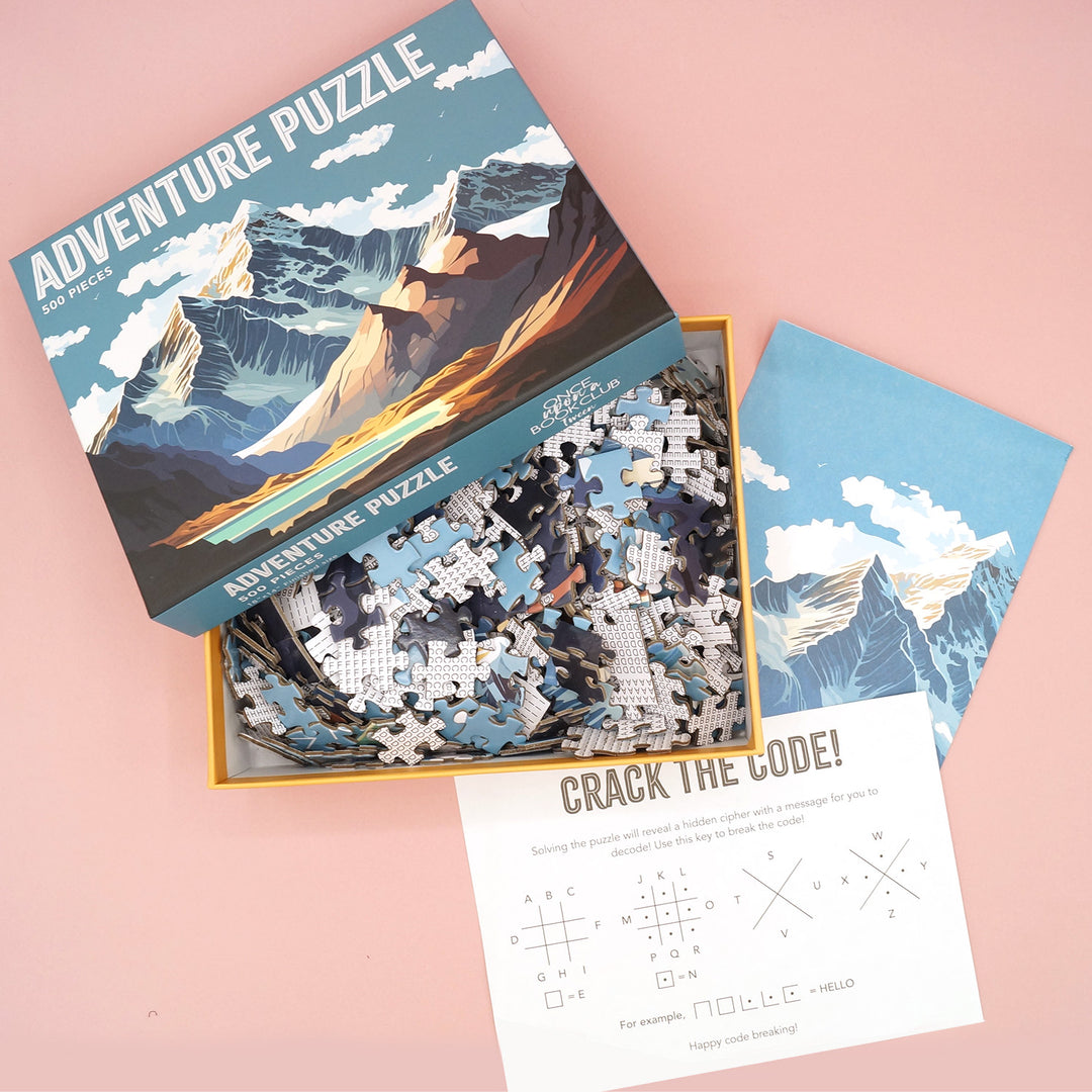 An open Adventure Puzzle box with a pile of puzzle pieces, a photo of the completed puzzle, and a piece of paper that says Crack the Code