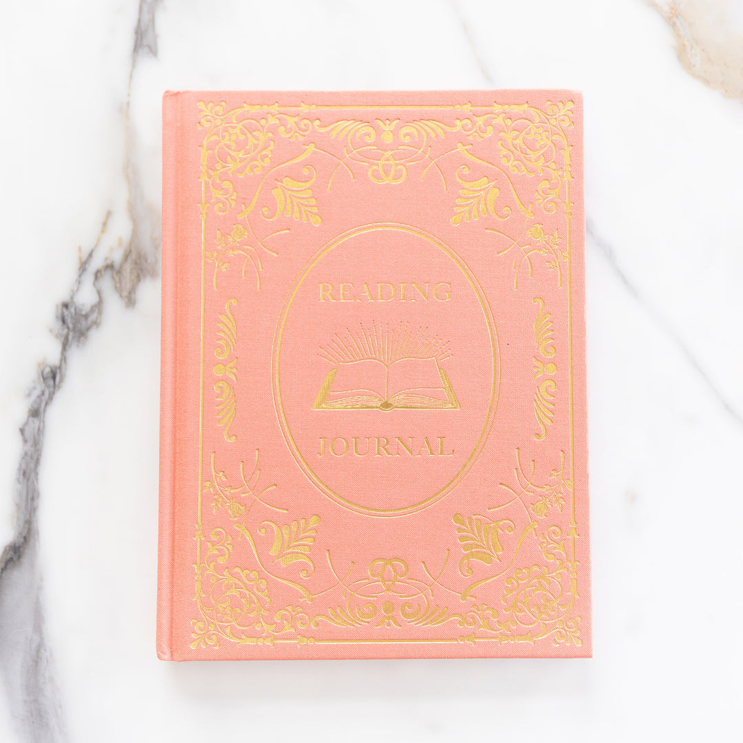 A flat lay of the coral and gold reading journal on a marble countertop.