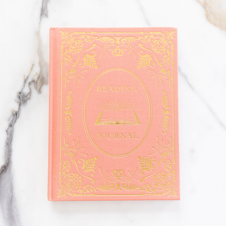 A flat lay of the coral and gold reading journal on a marble countertop.