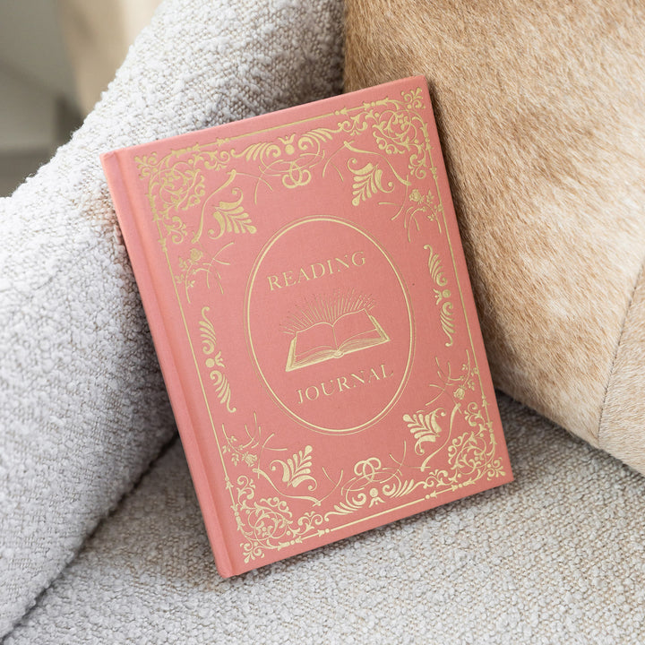 A coral and gold reading journal sits on a beige armchair.