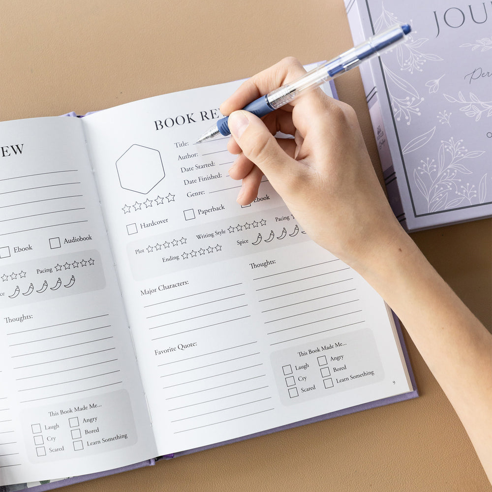 The inside of the reading journal showcasing the book review page details. A hand holds a pen over the page, preparing to write.