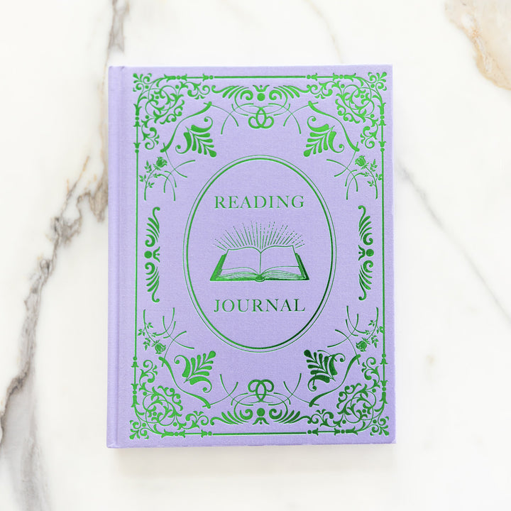 A flat lay of the periwinkle purple and green reading journal on a marble countertop.