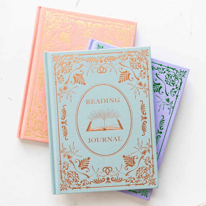 All three reading journal colorways sit in a stack on a white marble counter.