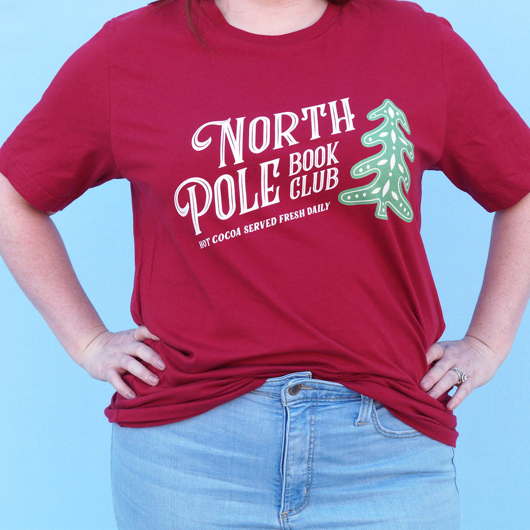 Person wearing a red t-shirt with 'North Pole Book Club' design on a blue background