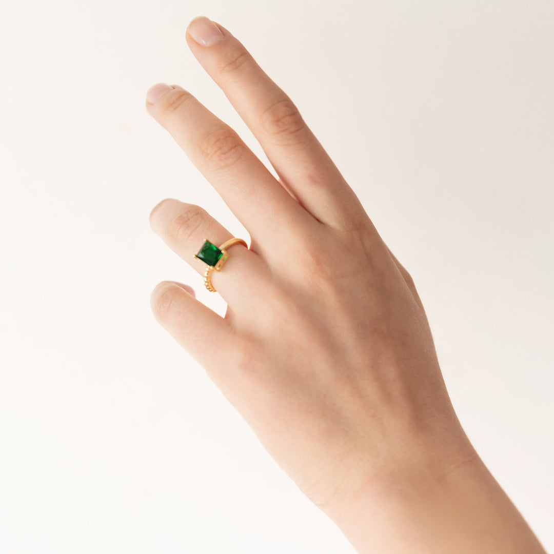 A white hand wears a green emerald ring with a gold band