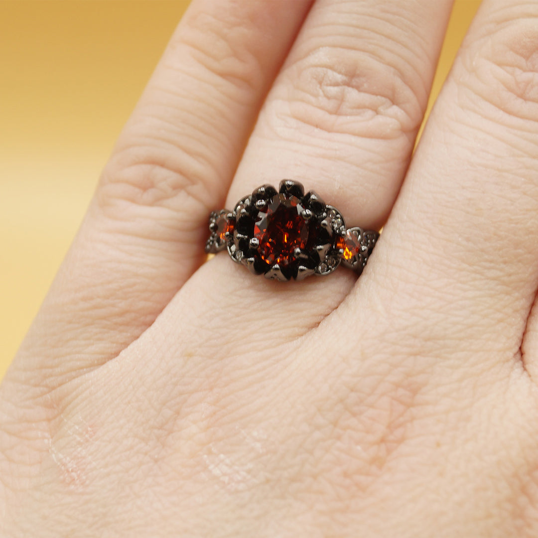 a white hand wears a black ring with a red gemstone in the center